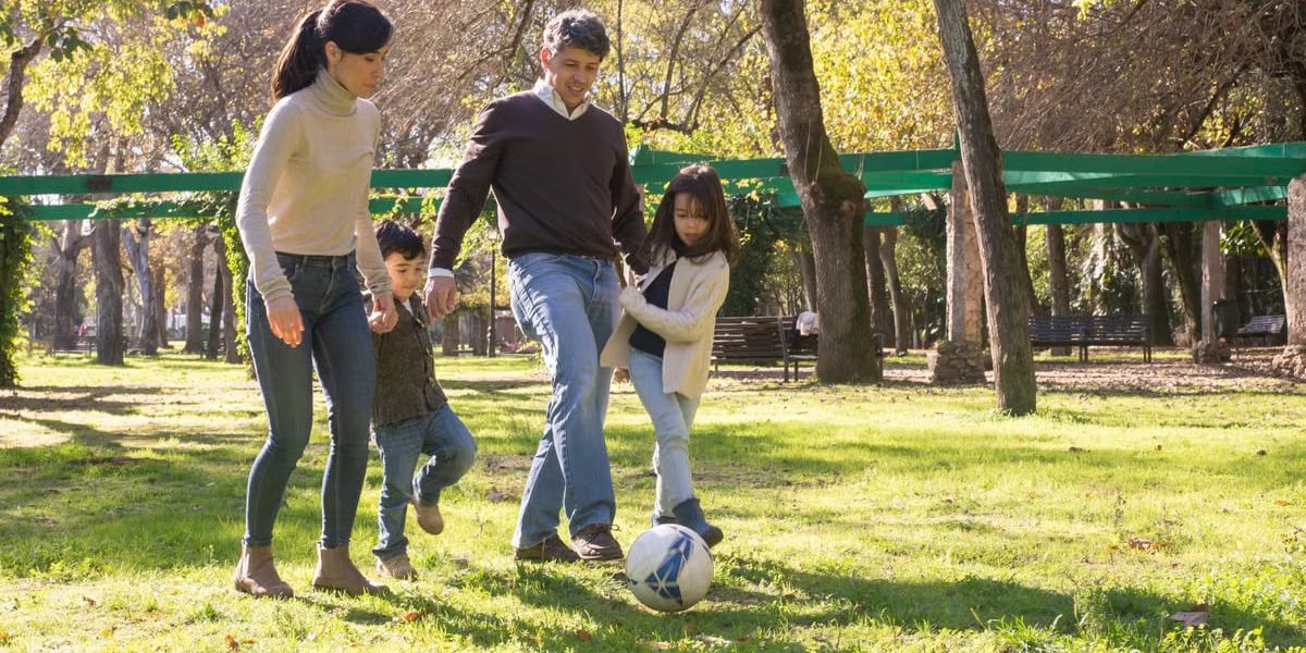 A family plays soccer together in a sunny park, enjoying quality time outdoors.