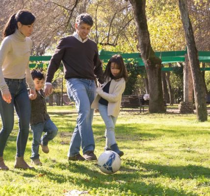 A family plays soccer together in a sunny park, enjoying quality time outdoors.