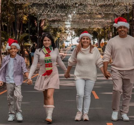 A joyful family walks down a decorated street wearing Christmas hats, symbolizing holiday spirit.